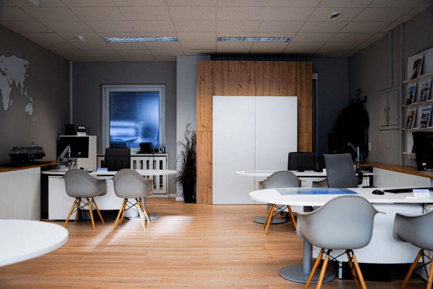 Modernes Reisebüro mit weißen runden Tischen und heller Einrichtung.